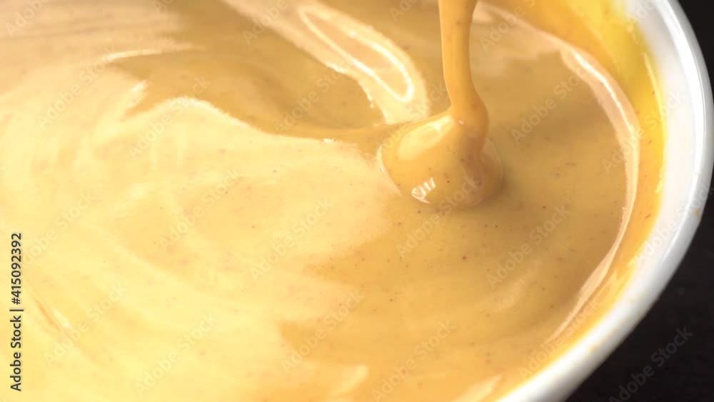Slow motion closeup view of spoon stirring sweet delicious looking custard cream. Sauce dripping from spoon into ceramic glass. Slow motion closeup view of spoon stirring sweet delicious looking custard cream. Sauce dripping from spoon into ceramic glass.
