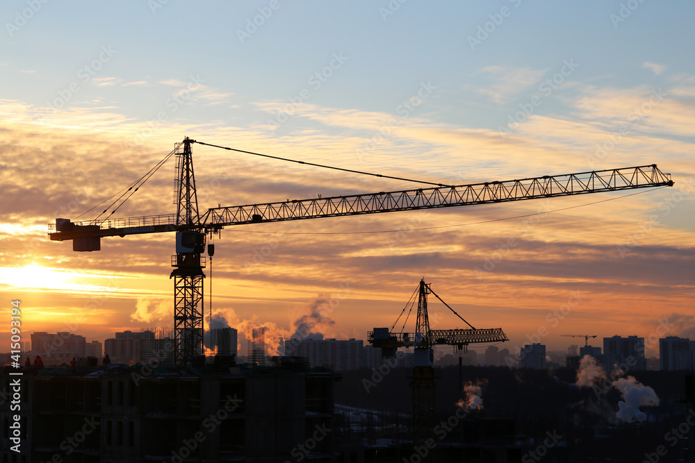 Construction cranes and unfinished residential buildings in sunshine. Housing construction, real estate, apartment block in city