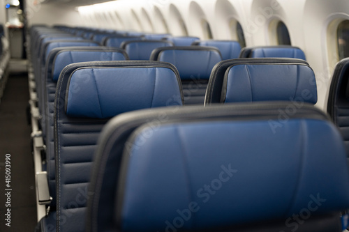 Rows of empty blue leather seats on a commercial airplane.
