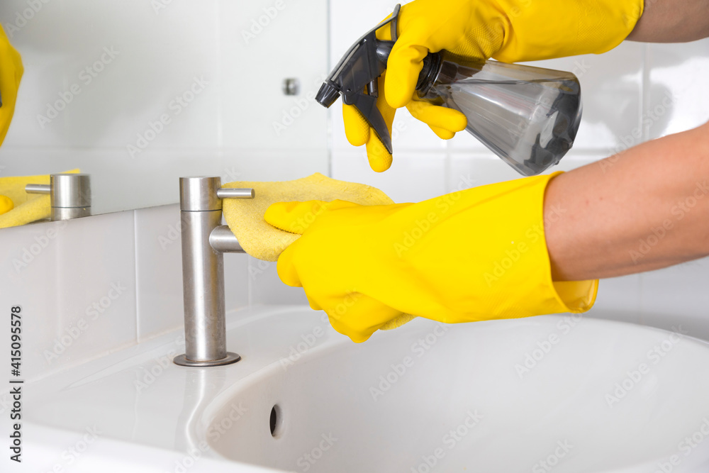 Yellow gloves cleaning sink in the bathroom. Disinfecting the bathroom. Prevention of coronavirus infection.