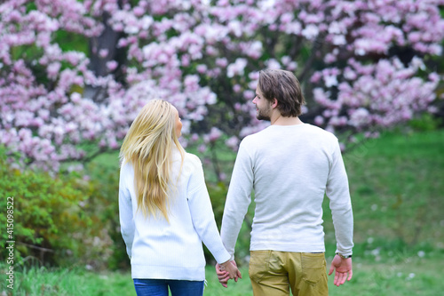 Couple hold hands in spring park, back view. Woman and man date in blossoming garden. Spring, nature awakening, beauty season. Love, romance, relations and family.