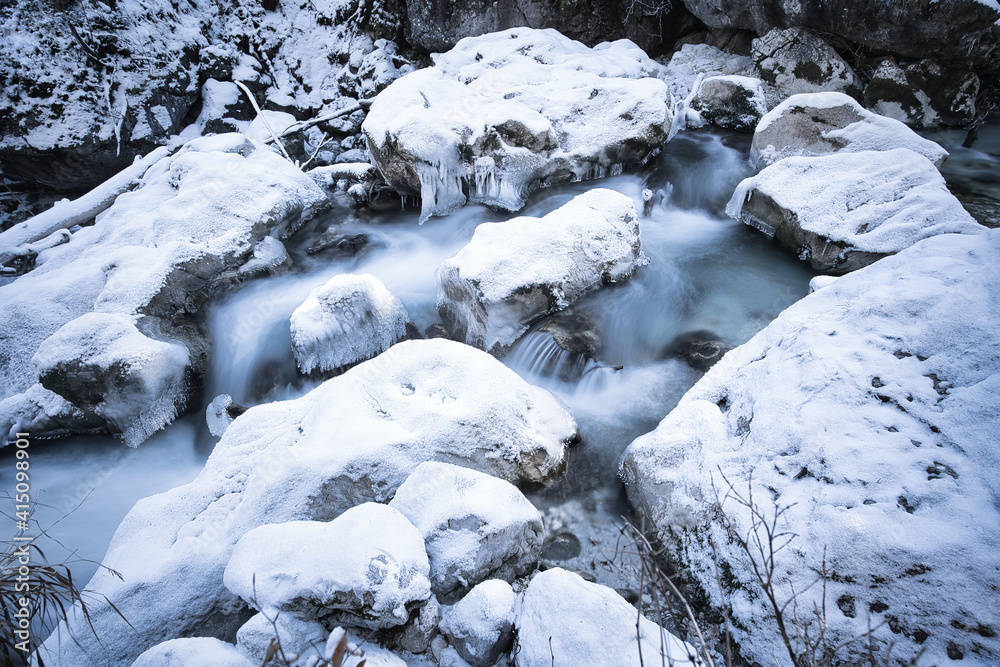 snow covered rocks in a river captured as smooth long exposure; winter landscape