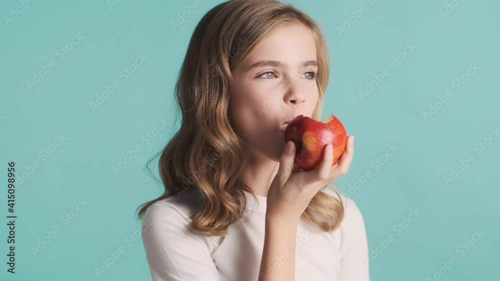 Pretty positive blond teenager girl eating apple looking happy over colorful background. Time for snack Pretty positive blond teenager girl eating apple looking happy over colorful background. Time for snack