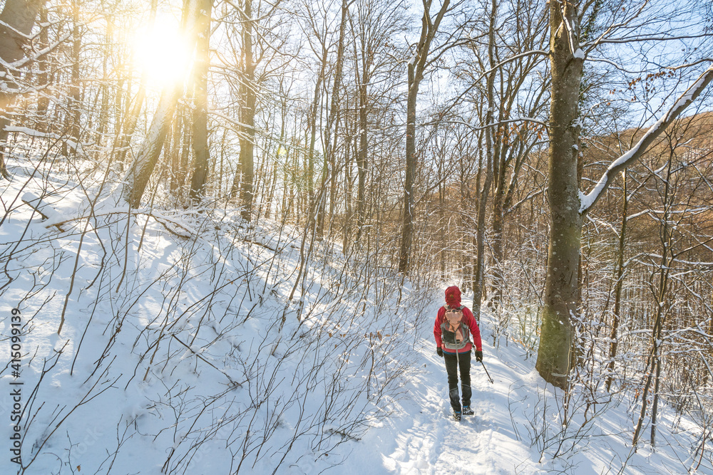 Man in outdoor gear with backpack hiking through snowy forest in the winter