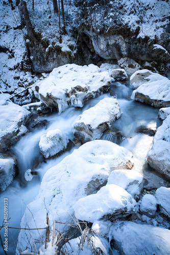 snow covered rocks in a river captured as smooth long exposure; winter landscape