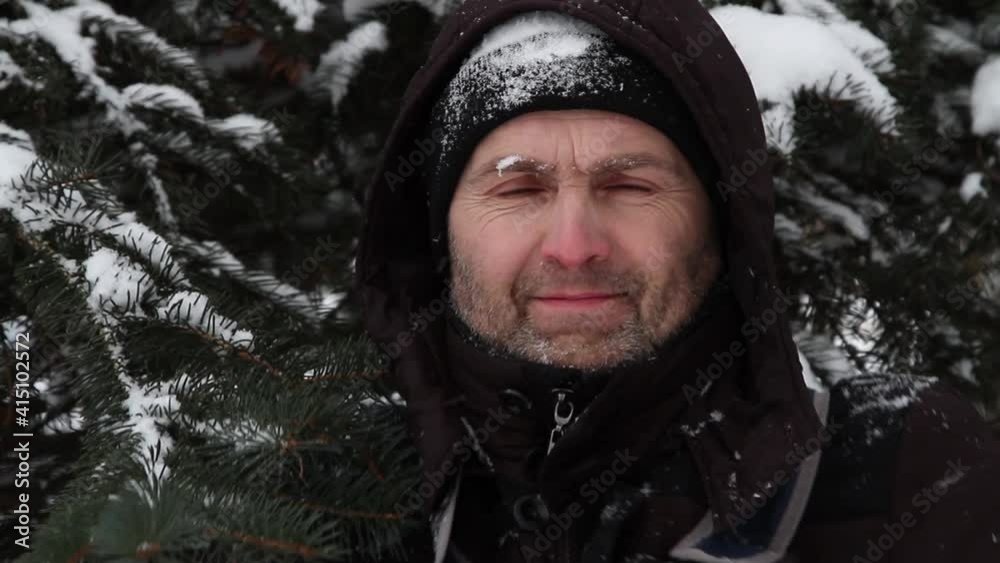 Portrait of a freezing and contented man against the background of snow-covered branches of a Christmas tree. Portrait of a freezing and contented man against the background of snow-covered branches of a Christmas tree.