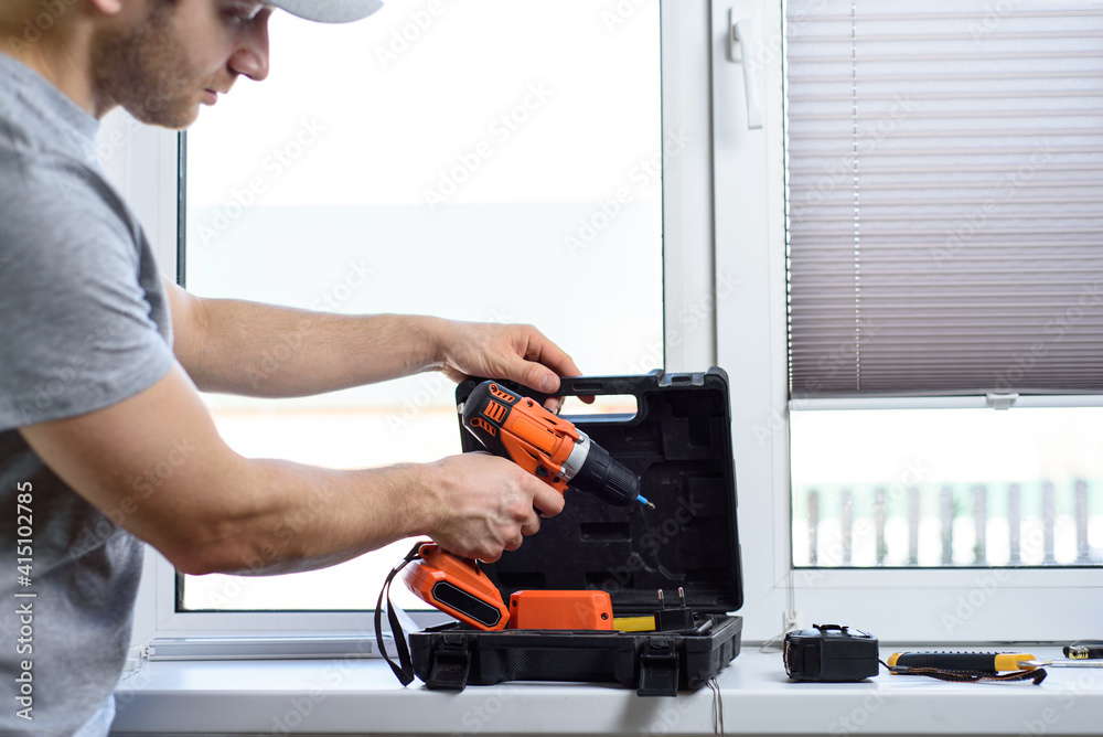 Man installing gray pleated blinds on the window with screwdriver Man installing gray pleated blinds on the window with screwdriver
