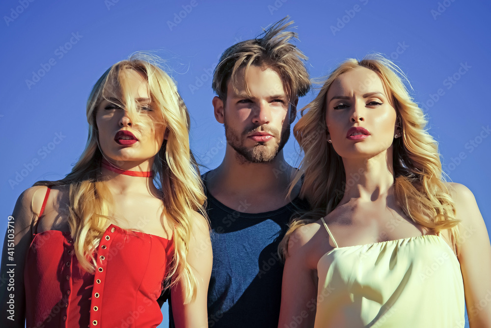 Twins women with sexy man on blue sky background. Love triangle and romance. Beauty and summer fashion. Polygamy betrayal and swinger. Twins women with sexy man on blue sky background. Love triangle and romance. Beauty and summer fashion. Polygamy betrayal and swinger.