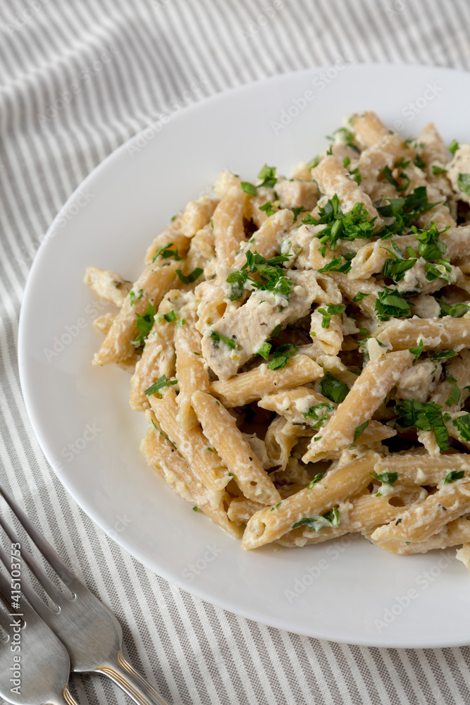 Homemade Chicken Alfredo Penne with Parsley on a white plate, side view.