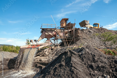 Wheel loader in operation in an industrial mining area (loads gold-bearing mountain soil into the hopper of an industrial washing device). Mining