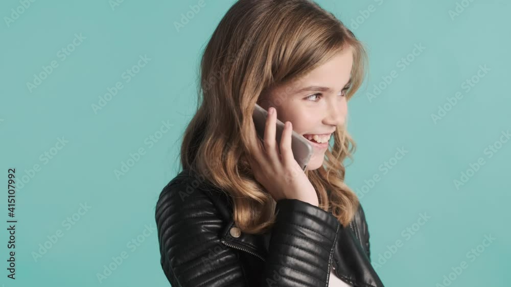 Beautiful stylish blond teenage girl dressed in leather jacket talking on phone over blue background. Distant communication Beautiful stylish blond teenage girl dressed in leather jacket talking on phone over blue background. Distant communication
