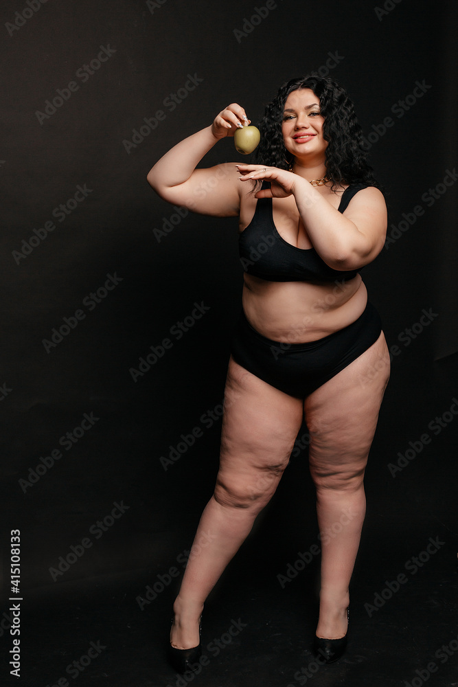 Obraz premium Plus size model in lingerie, fat sexy woman in underwear on black studio background, body positive concept, full length portrait,a beautiful plus size model holds an apple in her hand