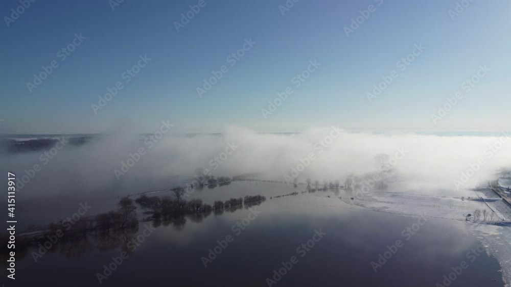 Foggy winter sunrise over the river IJssel with a high water level and ice and snow during a cold day in The Netherlands. Aerial drone point of view. Foggy winter sunrise over the river IJssel with a high water level and ice and snow during a cold day in The Netherlands. Aerial drone point of view.