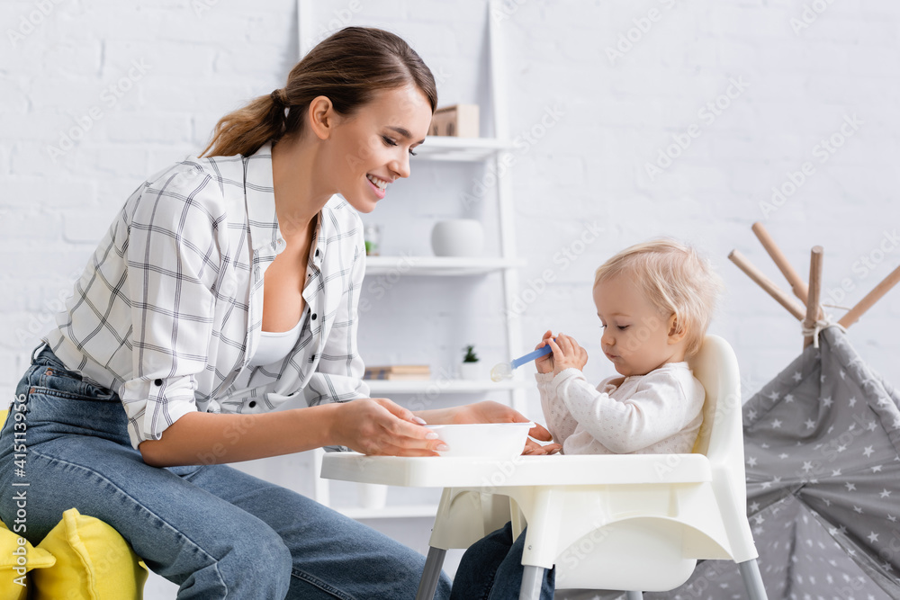 little boy sitting on kids chair with spoon near happy mother little boy sitting on kids chair with spoon near happy mother