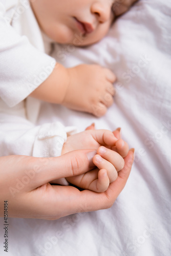 woman touching hand of little son sleeping on white bedding, blurred background © LIGHTFIELD STUDIOS