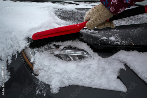 Hand of woman using brush and remove snow and ice from car and windscreen, concept of transportation and winter