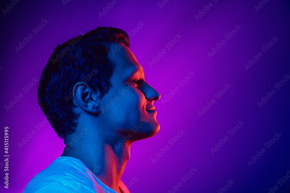 Caucasian man's portrait on purple blue studio background in multicolored neon light. Beautiful male model. Concept of human emotions, facial expression, sales, ad, fashion. Copyspace. - obrazy, fototapety, plakaty 