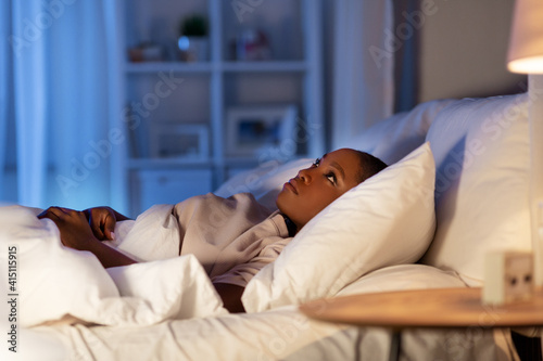 people, bedtime and rest concept - sleepless african american woman lying in bed at night and looking up photo