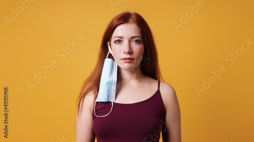 Fényképezés young woman with medical face mask hanging from her ear - improper use of protec