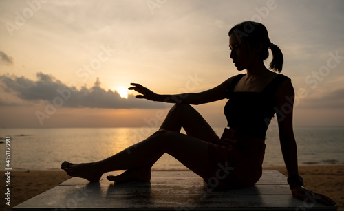 Woman silhouette sitting on the beach stand with beautiful sunset.