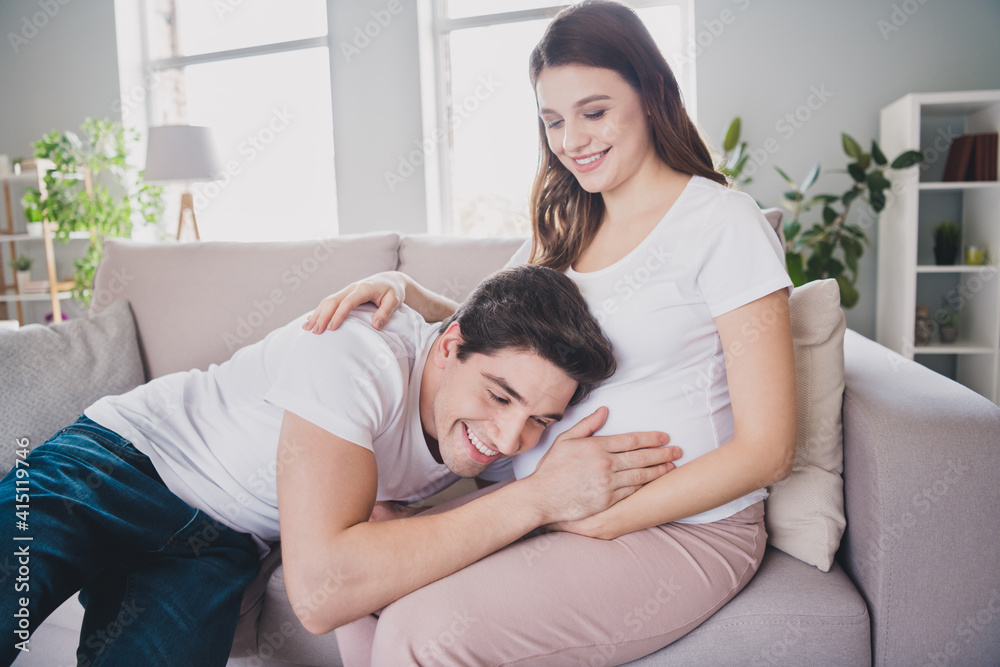 Portrait of attractive cheery tender sweet spouses sitting on couch waiting baby guy listening tummy in light house flat indoor Portrait of attractive cheery tender sweet spouses sitting on couch waiting baby guy listening tummy in light house flat indoor