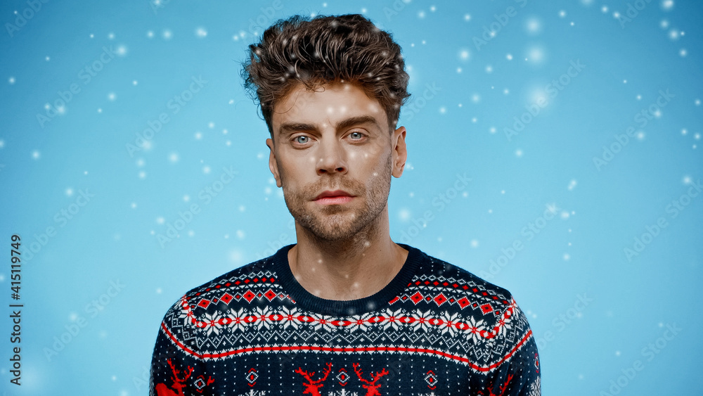 Man in sweater looking at camera under falling snow on blue background Man in sweater looking at camera under falling snow on blue background