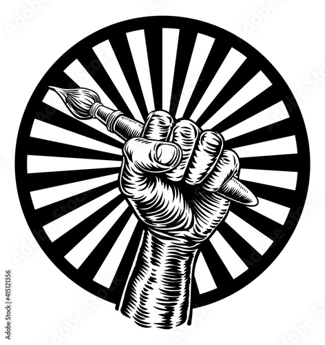 A fist hand holding an artists paintbrush in a vintage intaglio woodcut engraved or retro propaganda style