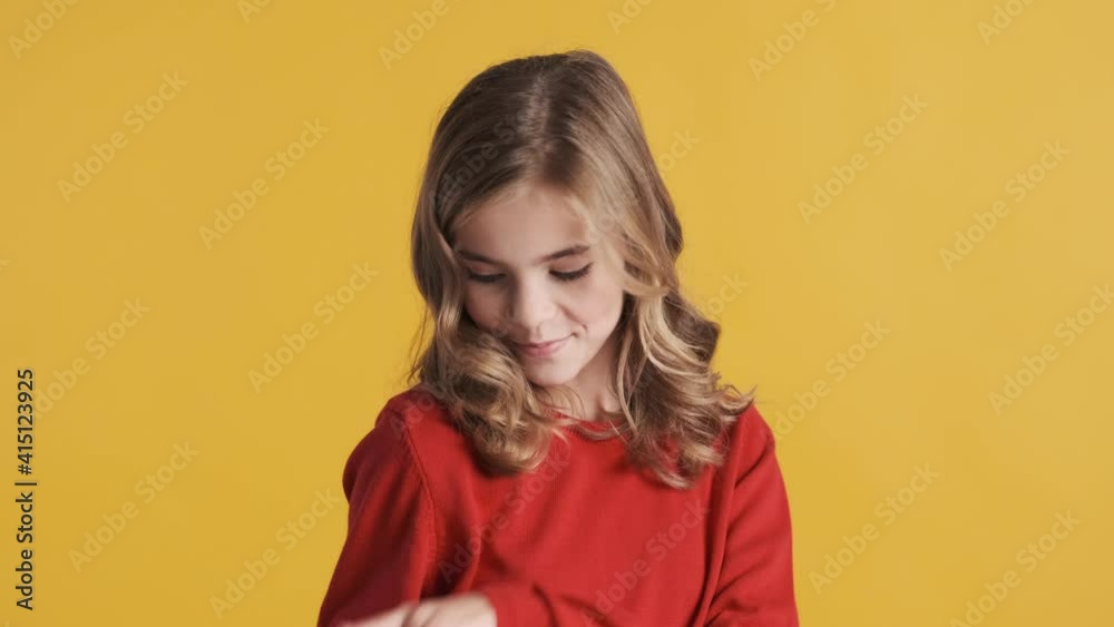 Attractive blond teenager girl dressed in red sweater dancing while posing on camera over yellow background