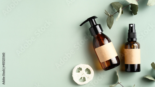 Natural skincare SPA cosmetics bottles, loofah and eucalyptus leaves on green background. Beauty salon banner mockup. Top view with copy space.
