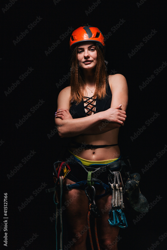 A girl in climbing gear poses against a black background