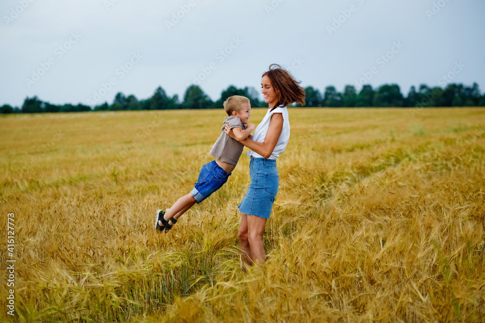 A happy family of mother and son in a summer wheat field. A woman holds her son in her arms and circles.