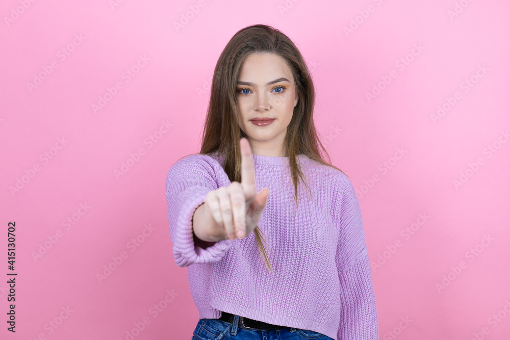 Young pretty woman with long hair standing over isolated pink background showing and pointing up with fingers number one while is serious Young pretty woman with long hair standing over isolated pink background showing and pointing up with fingers number one while is serious