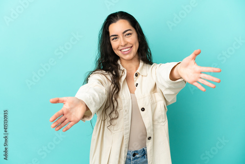 Young caucasian woman isolated on blue background presenting and inviting to come with hand