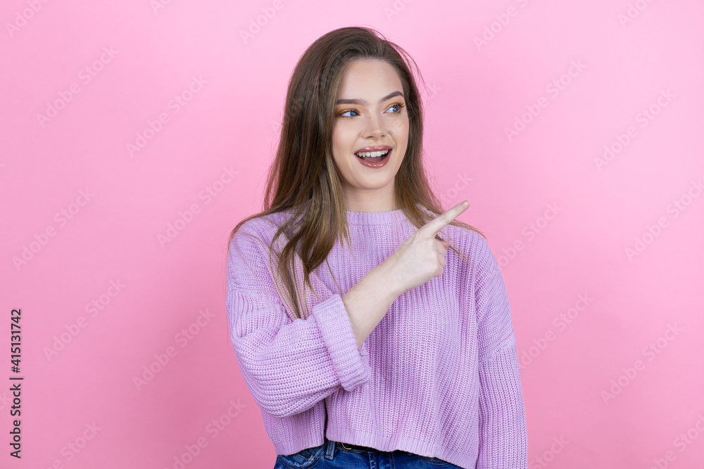 Young pretty woman with long hair standing over isolated pink background smiling and pointing with hand and finger to the side Young pretty woman with long hair standing over isolated pink background smiling and pointing with hand and finger to the side