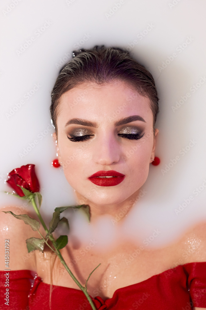 Beautiful young girl in a milk bath
holding a red rose. Relaxation concept. Women's Day 8 March.