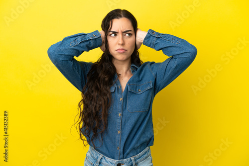 Young caucasian woman isolated on yellow background frustrated and covering ears © luismolinero