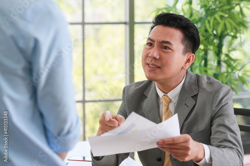 Asian businessman manager in suit holding paperwork and strong talking for young employee with anger and serious gesture look like he comments as disagree or unacceptable for his project work. photo