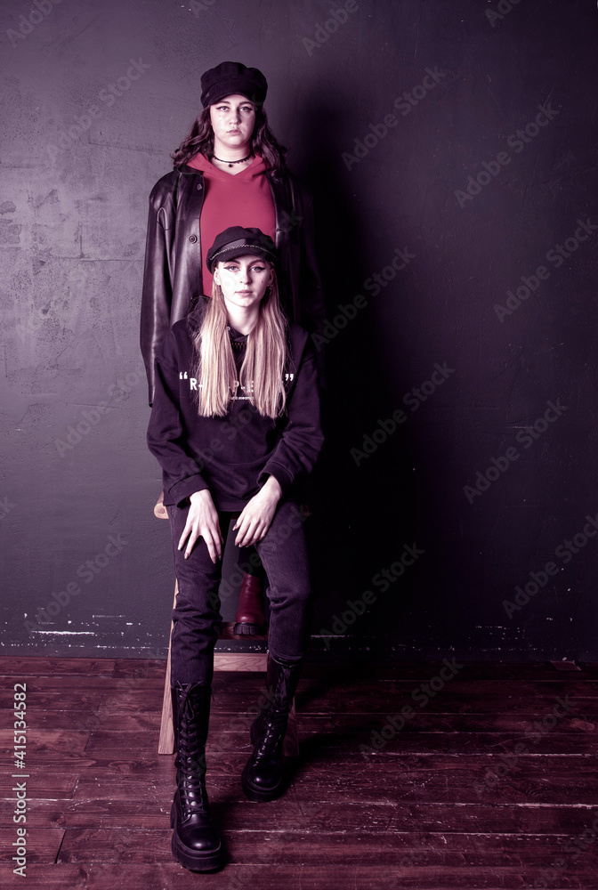 Obraz premium Two charming teenage girls with bright makeup, dressed in a grunge style, against a dark wall.
