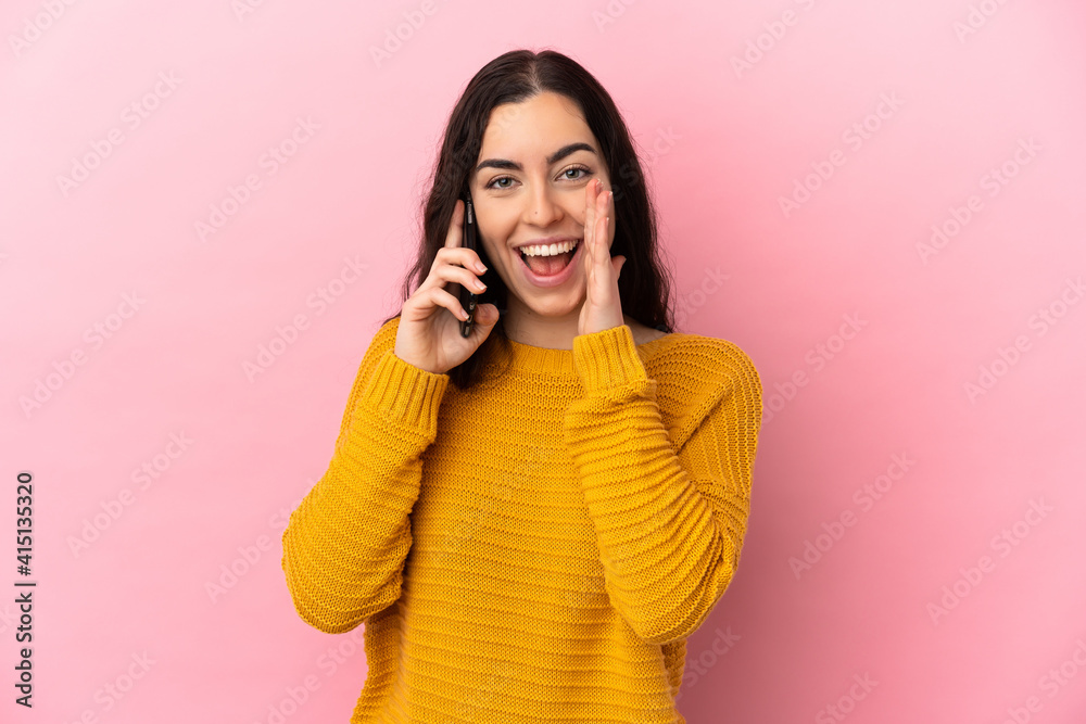 Young caucasian woman using mobile phone isolated on pink background shouting with mouth wide open Young caucasian woman using mobile phone isolated on pink background shouting with mouth wide open