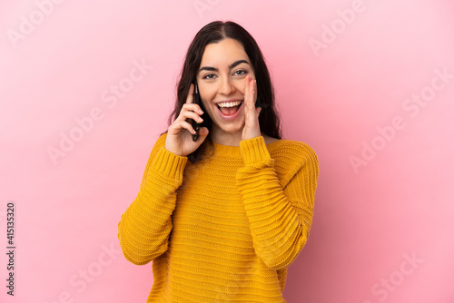 Young caucasian woman using mobile phone isolated on pink background shouting with mouth wide open