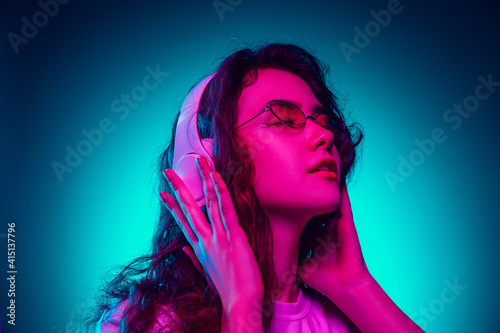 Dancing. Caucasian woman's portrait isolated on blue studio background in multicolored neon light. Beautiful female model. Concept of human emotions, facial expression, sales, ad, fashion. Copyspace.