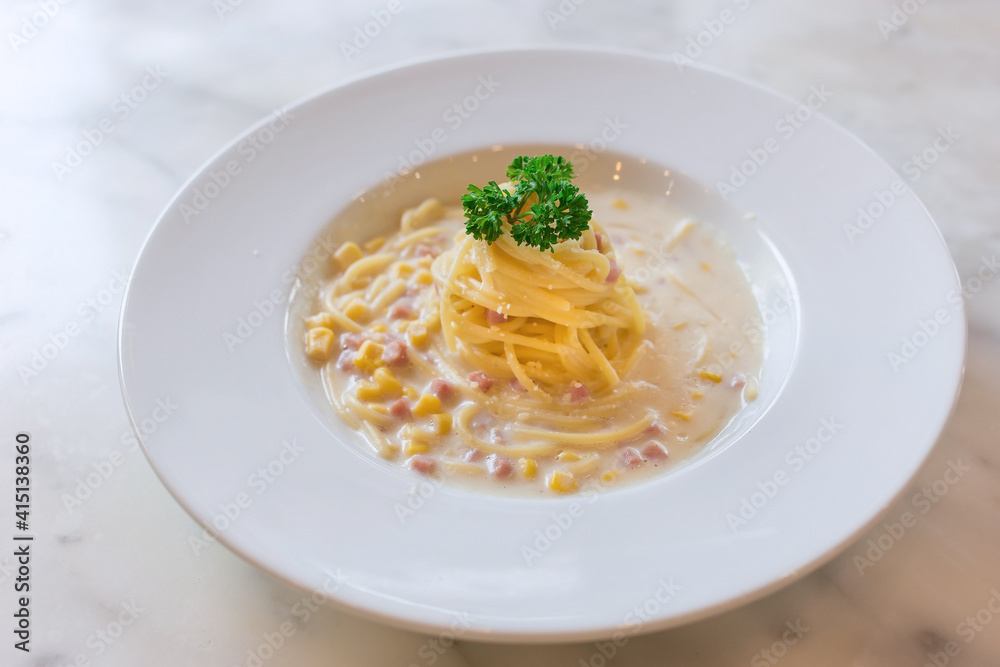 Spaghetti with ham and corn cream sauce put on a white plate on marble table as a background.