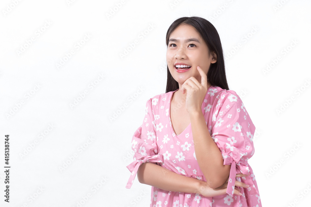 An Asian woman standing smiling in pink dress is looking at something while touching her face on a white background.