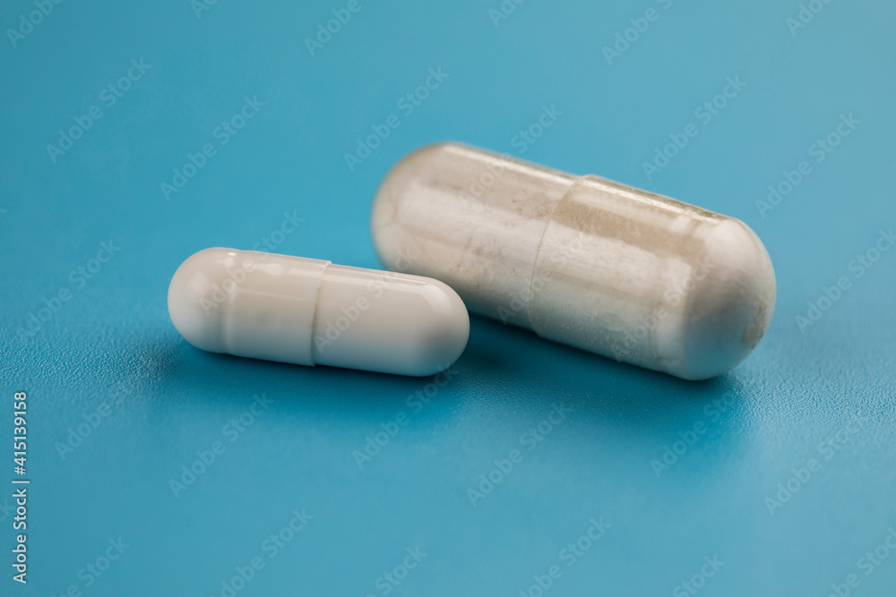 Two white pills capsule on blue background. Two white pills capsule on blue background.