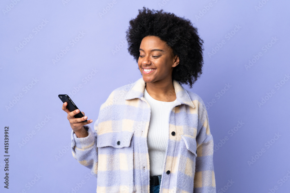 Young African American woman using mobile phone isolated on purple background with happy expression Young African American woman using mobile phone isolated on purple background with happy expression