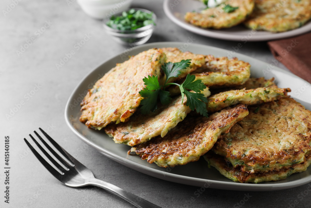 Delicious zucchini fritters served on grey table, closeup
