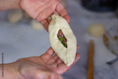 Close up view of pita, pitta bread with ground meat in a woman's hands with blurred bakckground in the kitchen. Preparation of homemade pastry by a lady. Selective focus. photo