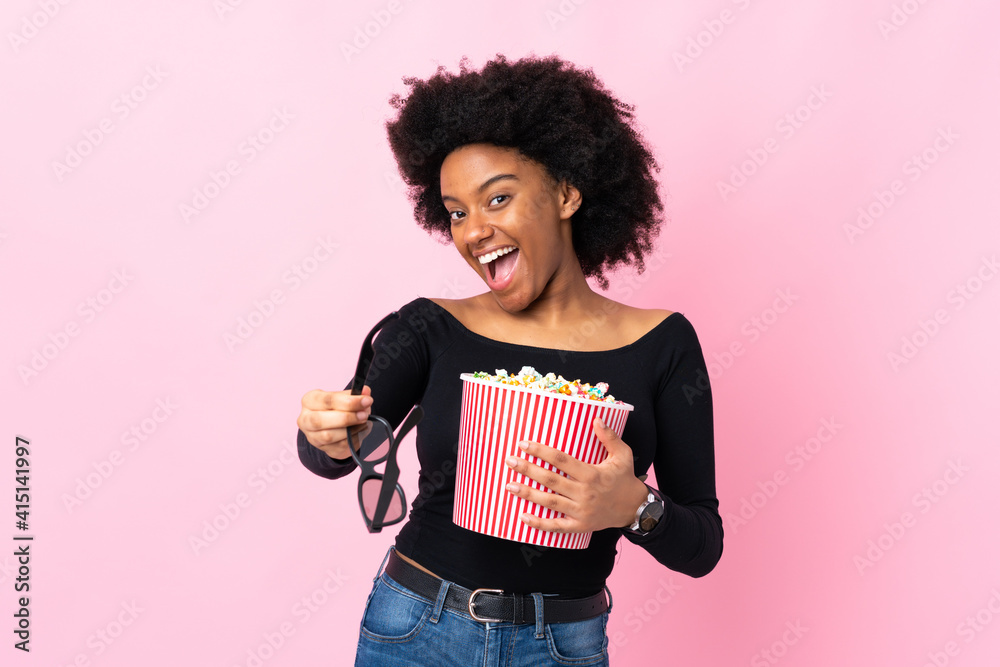 Young African American woman isolated on pink background with 3d glasses and holding a big bucket of popcorns Young African American woman isolated on pink background with 3d glasses and holding a big bucket of popcorns