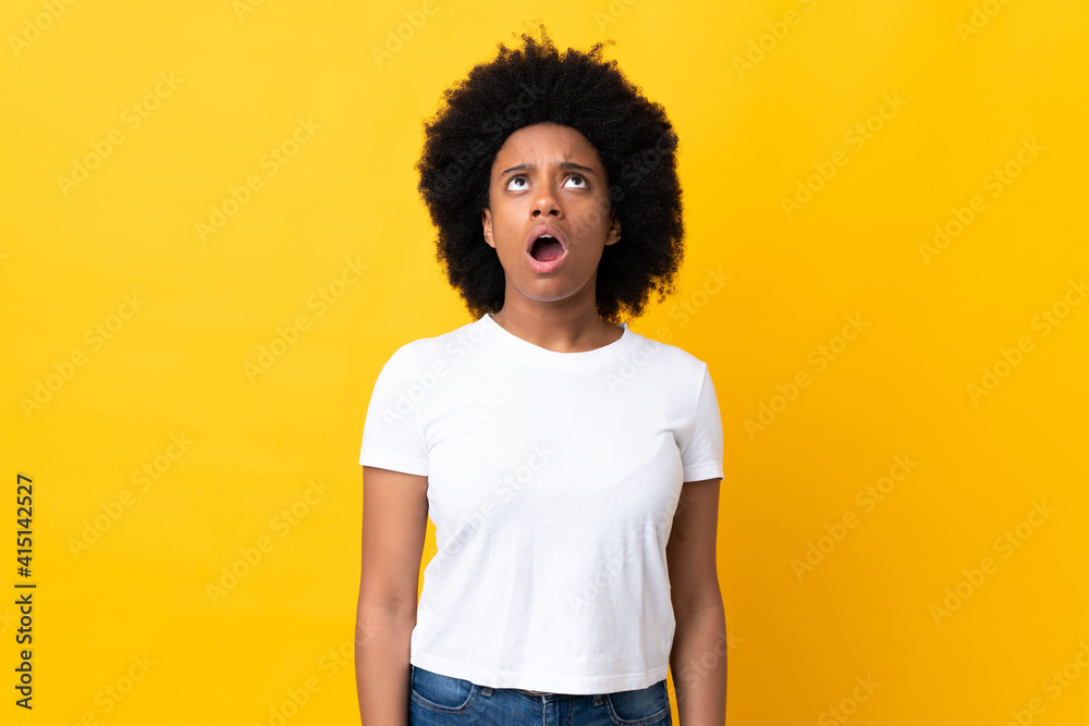 Young African American woman isolated on yellow background looking up and with surprised expression