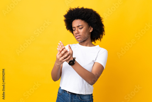 Young African American woman isolated on yellow background suffering from pain in hands